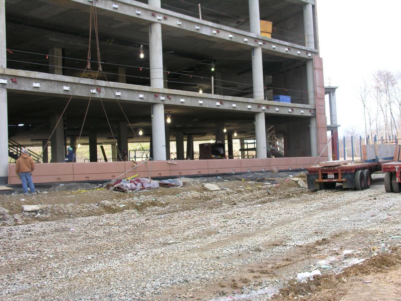 Beginnings of back wall and a closer view of the metal brackets. The flat bed trucks seen to the right in the picture bring in the concrete panels.