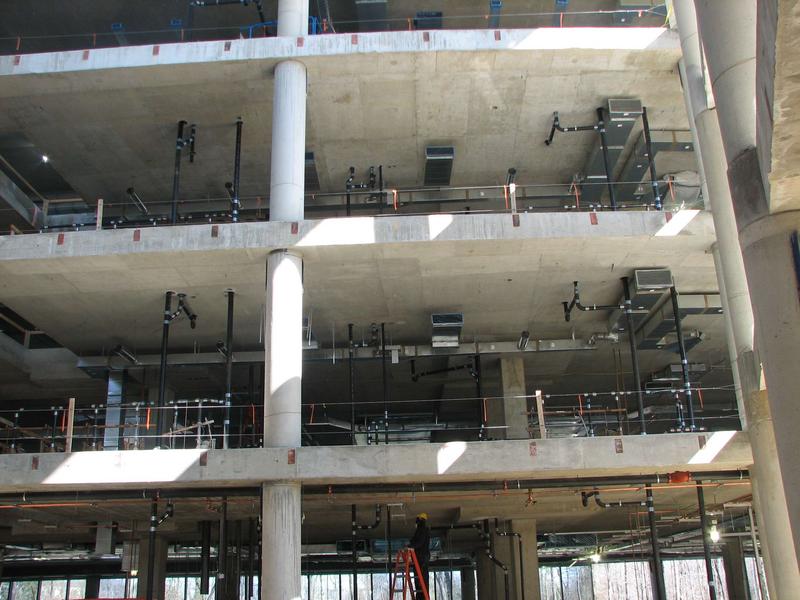 Interior view of first through third floor showing the vast network of pipes and duct work being installed.