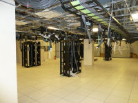 Inside the data center, where computer racks have been installed. Large bundles of cabling can be seen dangling from the ceiling, waiting for their racks to be installed. 
